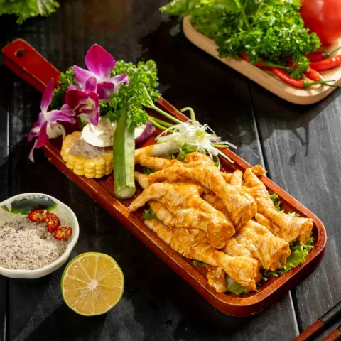 Chân gà nướng muối ớt vàng giòn trên thớt gỗ, kèm muối tiêu chanh và rau