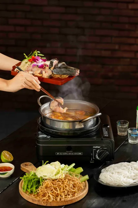 Gắp lát cá tầm nhúng vào nồi lẩu đang bốc khói trên bếp ga mini